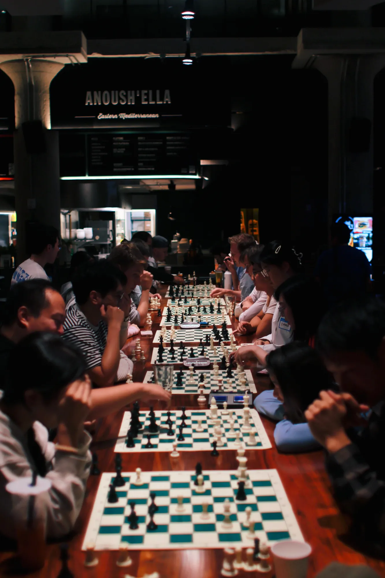 A dimly lit long table of chess games stretching into the distance
