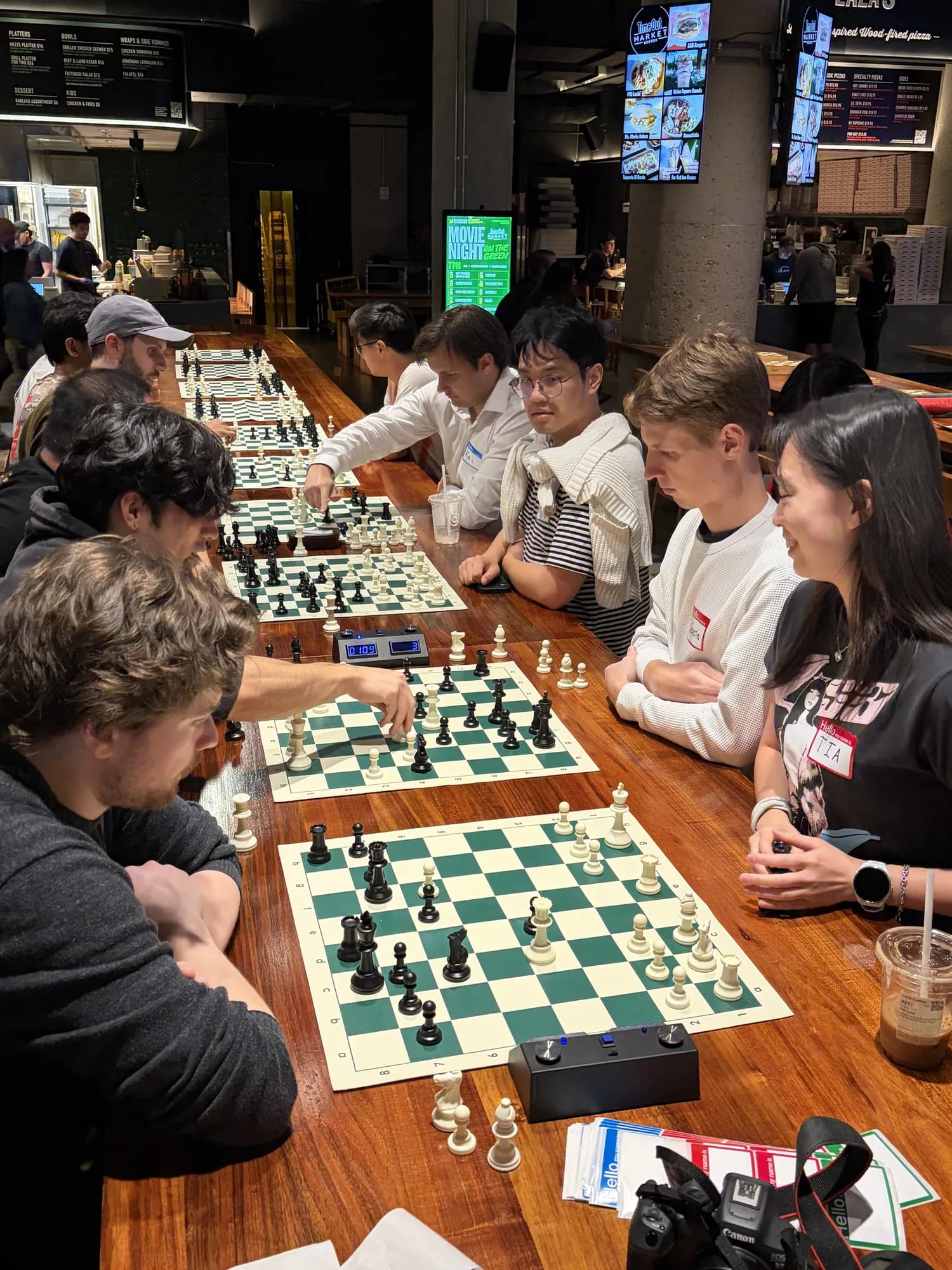 A long table lined with chess boards and players, seen from one end
