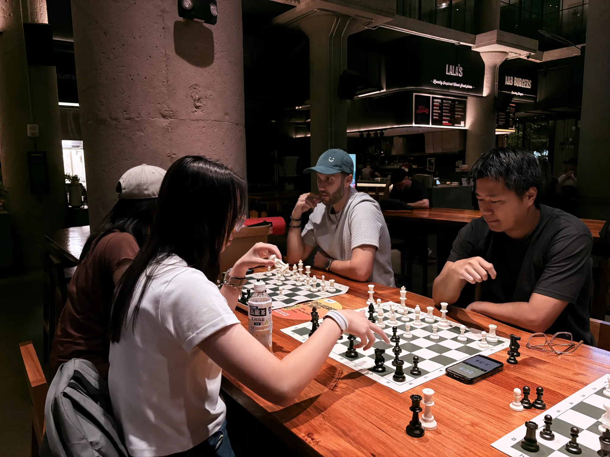 A player reaches to move a piece while two others watch the board