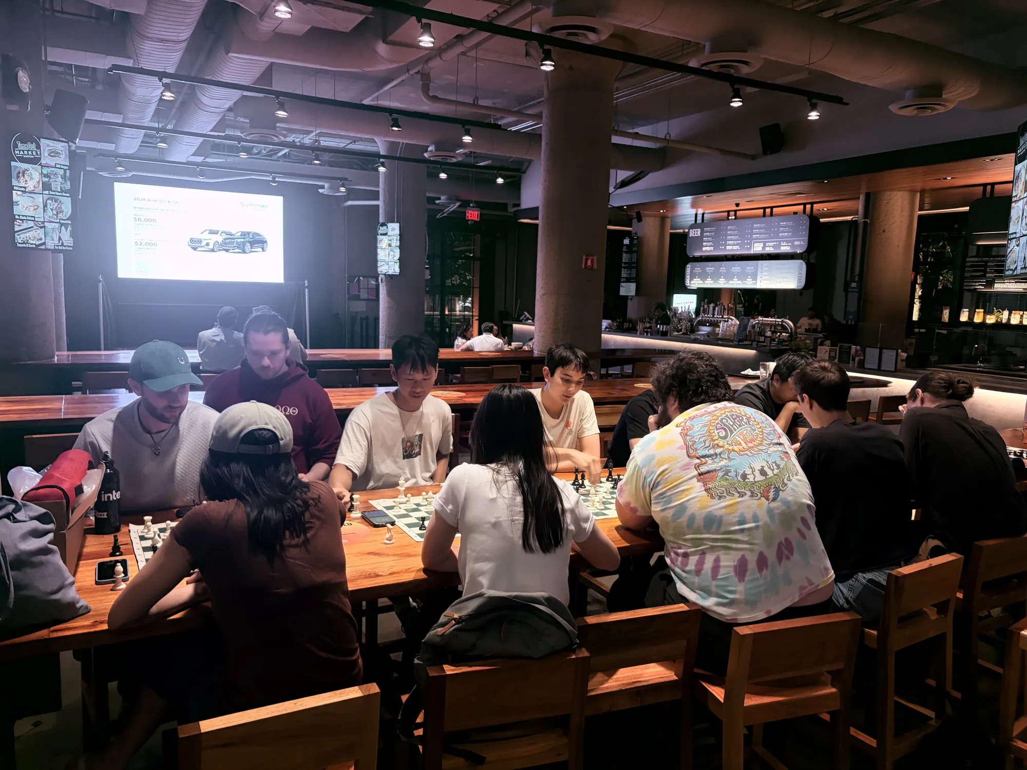 A full table of players gathered around chess boards under the food hall lights
