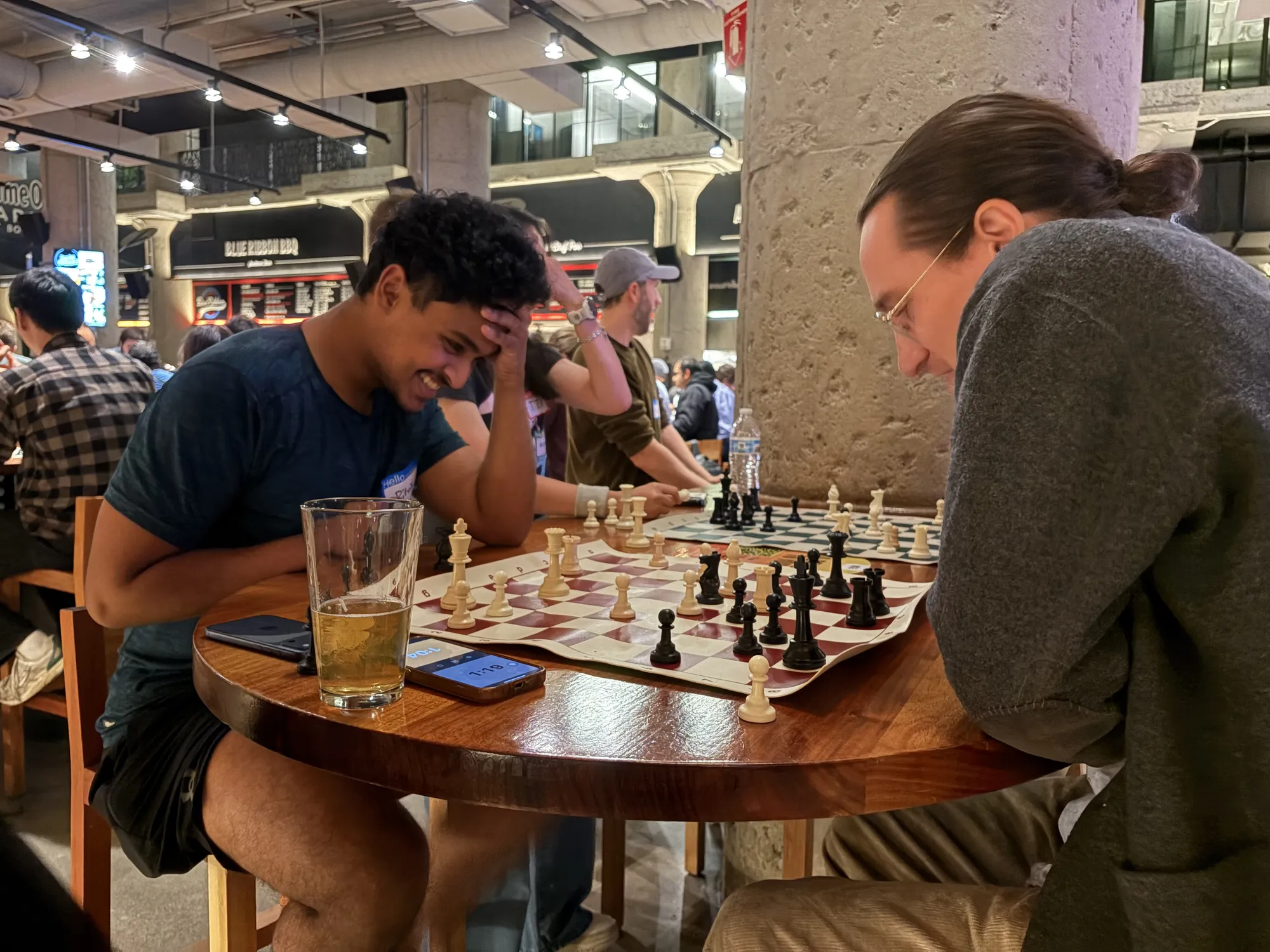 Two players grin over a game at a round table, with drinks beside the board
