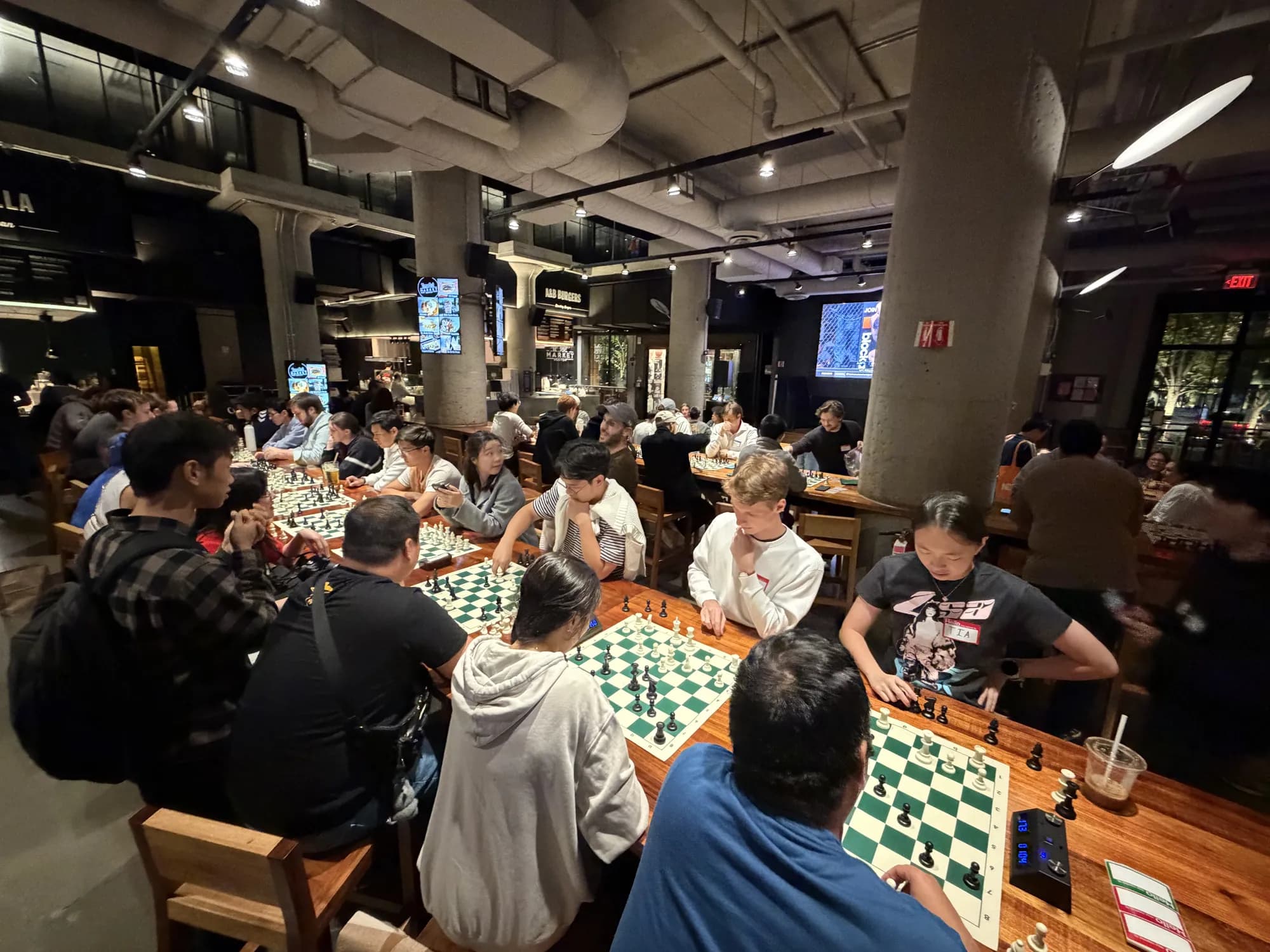 A packed room of tables with chess games in progress