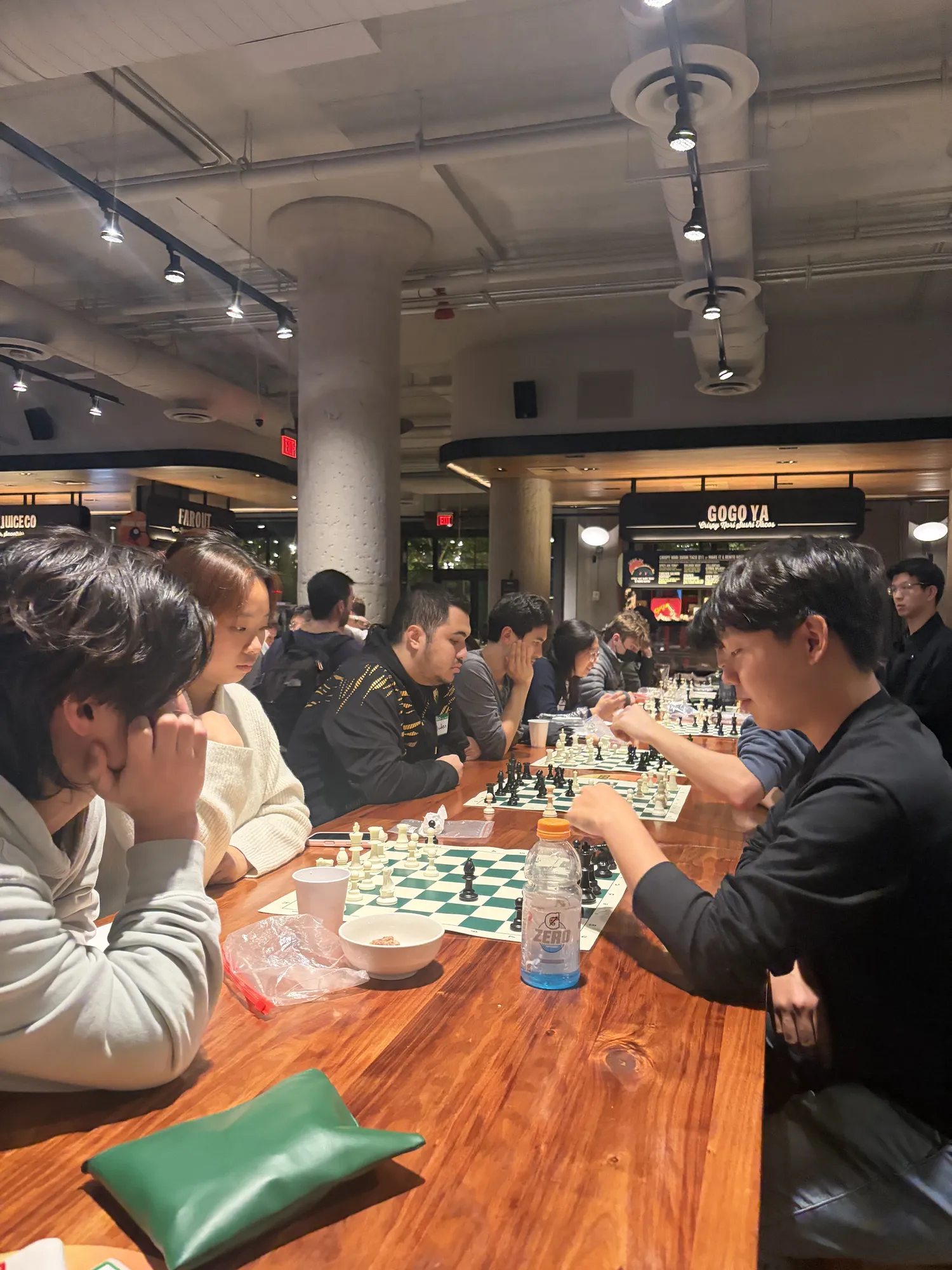 Players chat and play at a long table during a Tuesday chess night