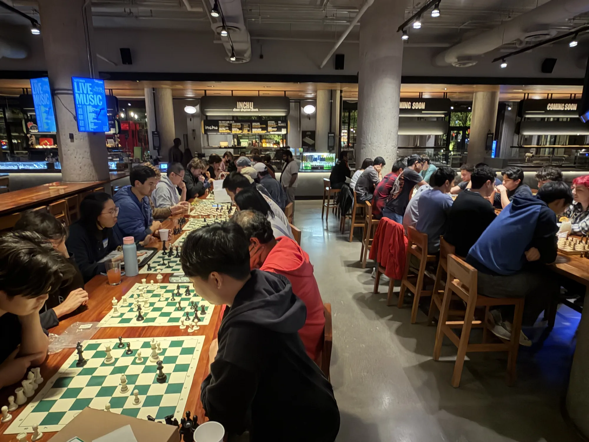 Dozens of players fill long tables of chess boards across the food hall