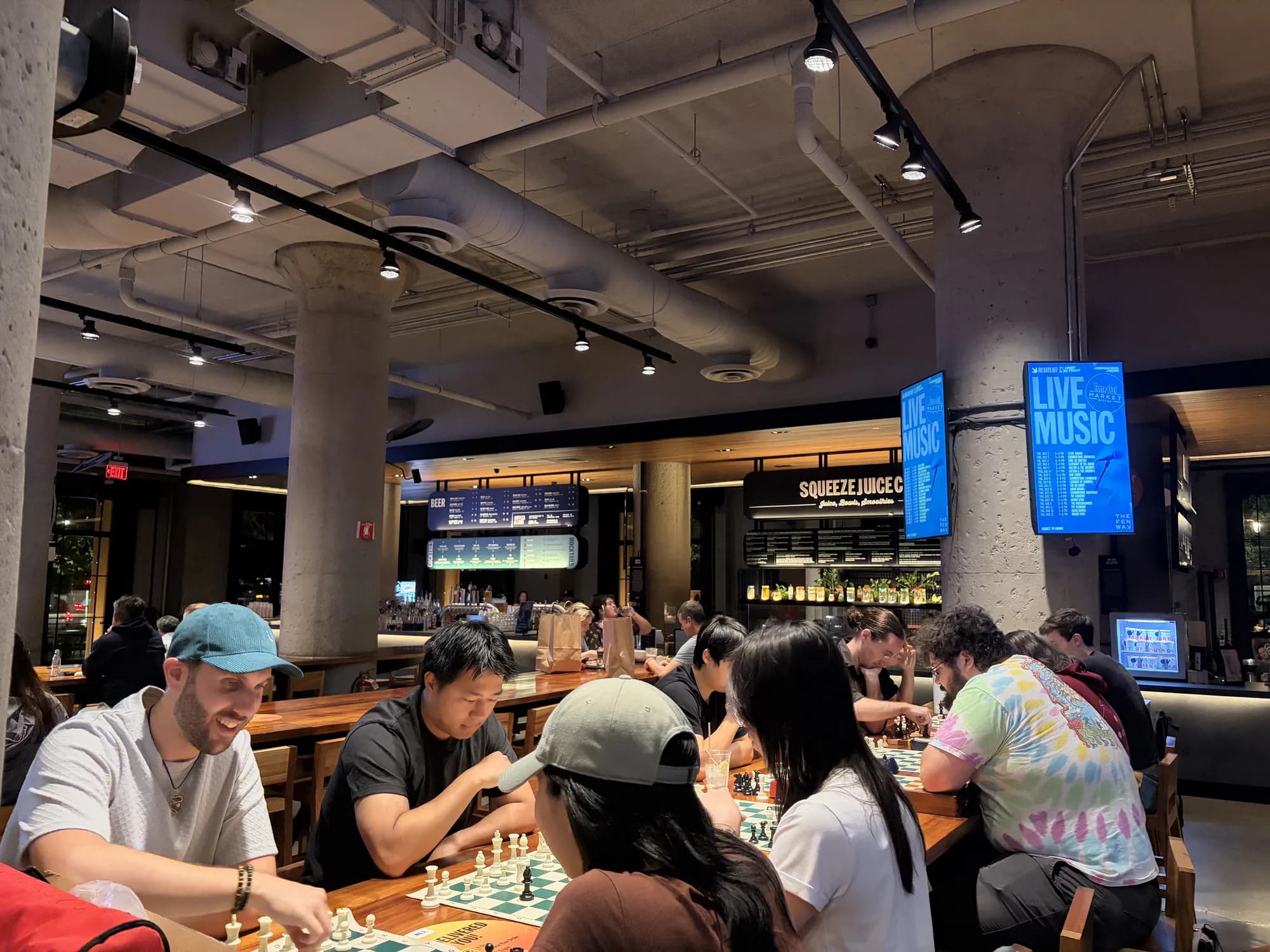Players smile over a game at a crowded table in the Time Out Market food hall